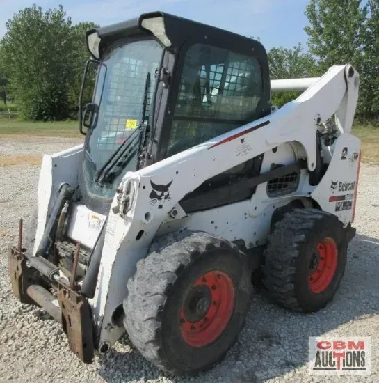 White Bobcat skid-steer loader with black cab, sitting on tires with red rims, outdoors.