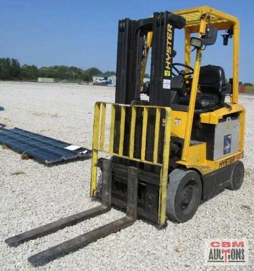Yellow Hyster forklift on gravel, with metal rails and long forks, outdoors on a sunny day.