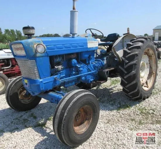 A blue ford tractor is parked in a gravel lot