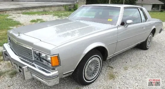 A silver car is parked on a gravel road.