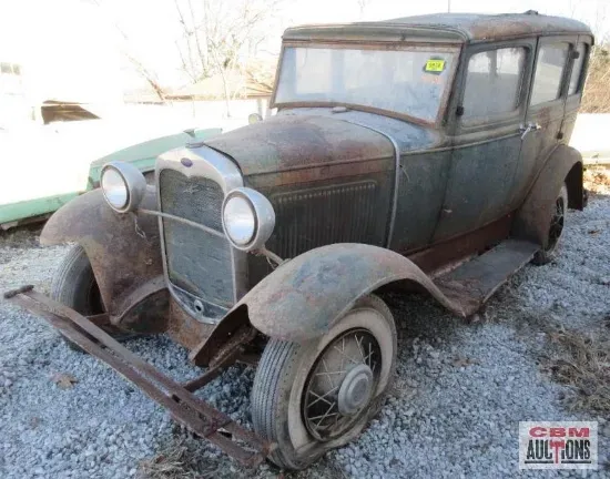 An old rusty car is parked in a gravel lot.