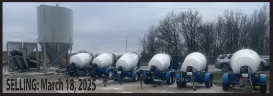 A row of concrete mixers are lined up in front of a silo.