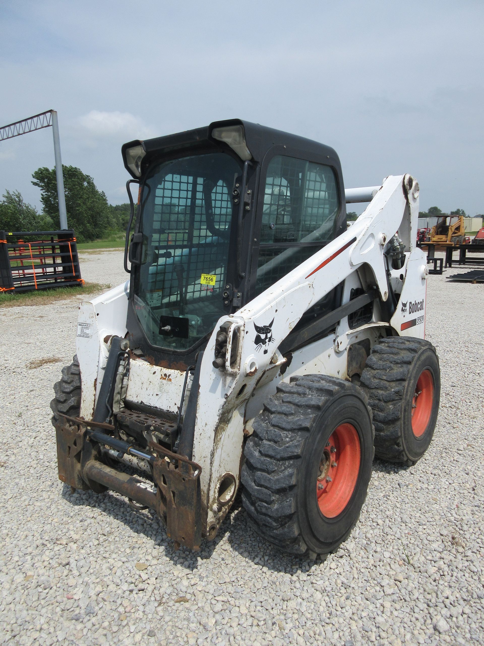 White Bobcat skid-steer loader with black cab parked on gravel lot.