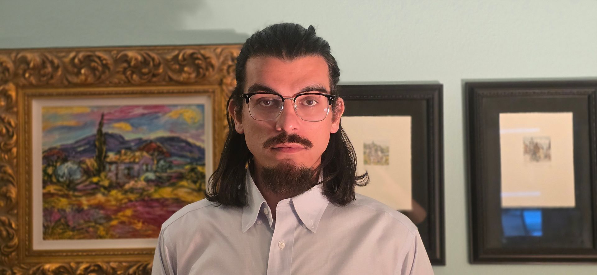 Owner of Agency standing indoors in front of framed artwork, wearing glasses and a white shirt.