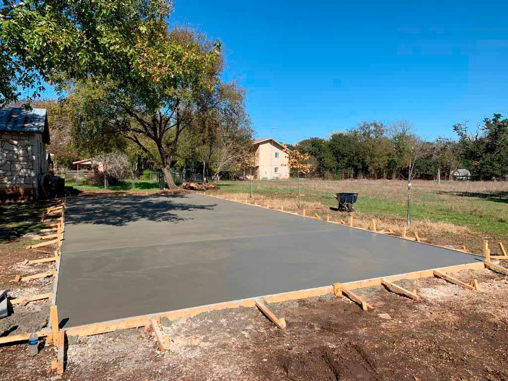 Freshly poured concrete slab with wooden formwork, outdoors in a grassy field.