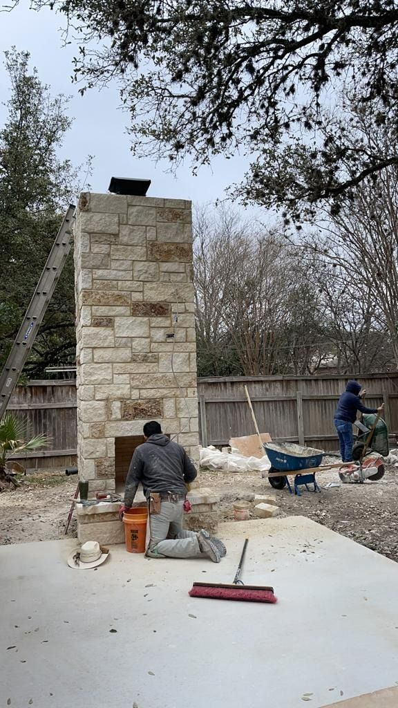Construction workers building a stone fireplace outdoors. One kneels; another mixes cement.