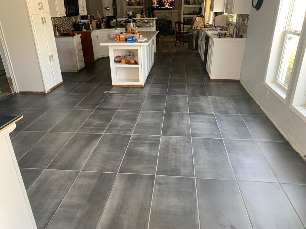 Gray tile floor in a kitchen with white cabinets, island, and windows.