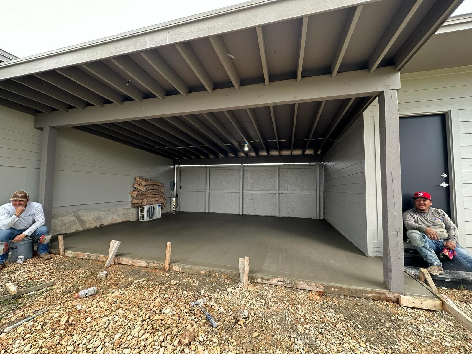 Concrete patio under a covered structure; two men seated; construction site.