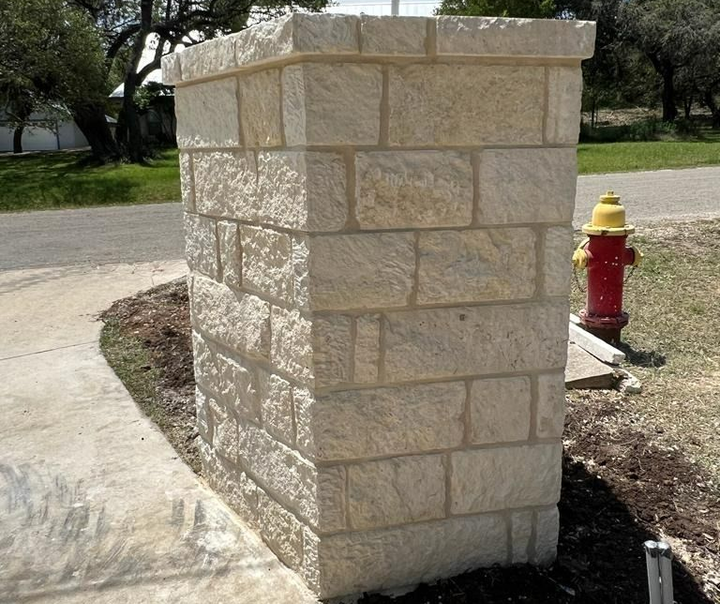 Stone pillar next to a sidewalk and a red fire hydrant, set in a yard.