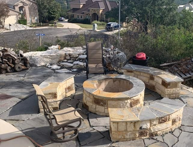 Patio with stone fire pit, built-in seating, and a single chair. Suburban setting with distant houses.