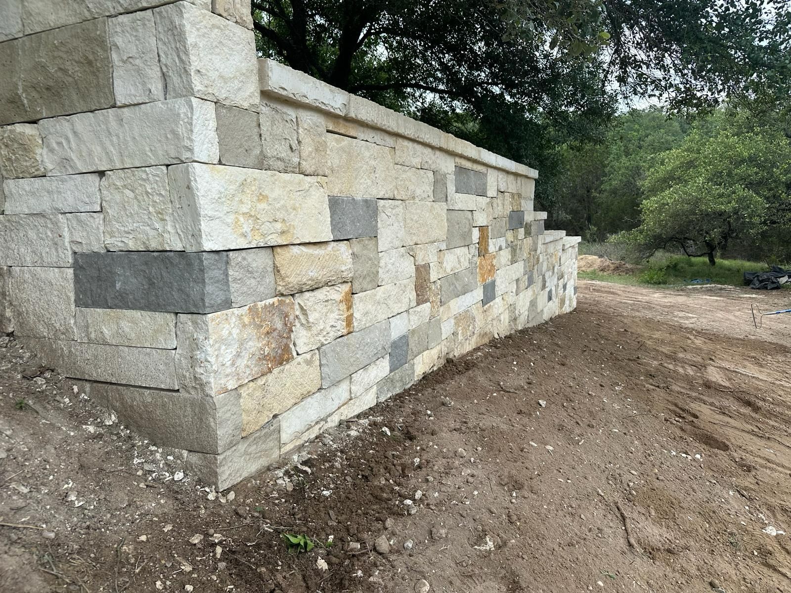Stone retaining wall, constructed with varying colored rectangular blocks, beside dirt.