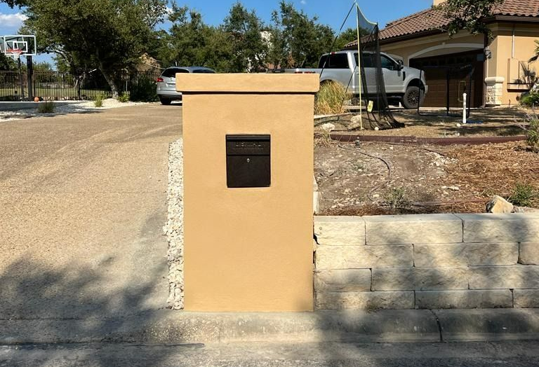 Tan mailbox pillar with black mailbox on a residential street.