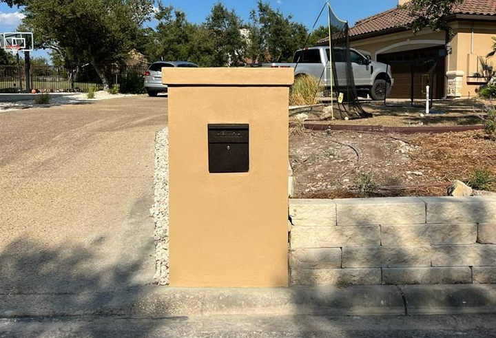 Tan mailbox pillar with black mailbox on a residential street.