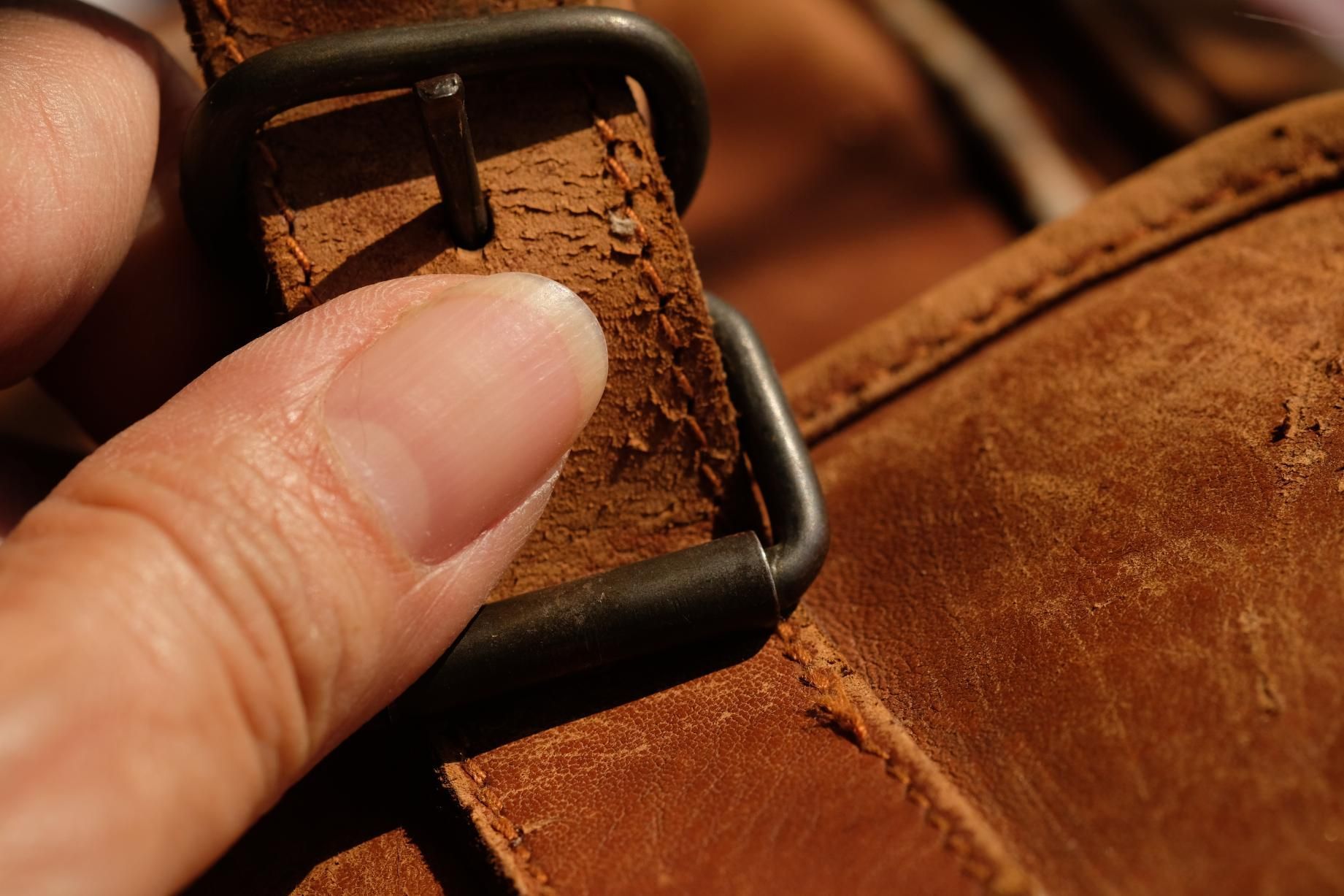 A person is holding a brown leather belt with a metal buckle.