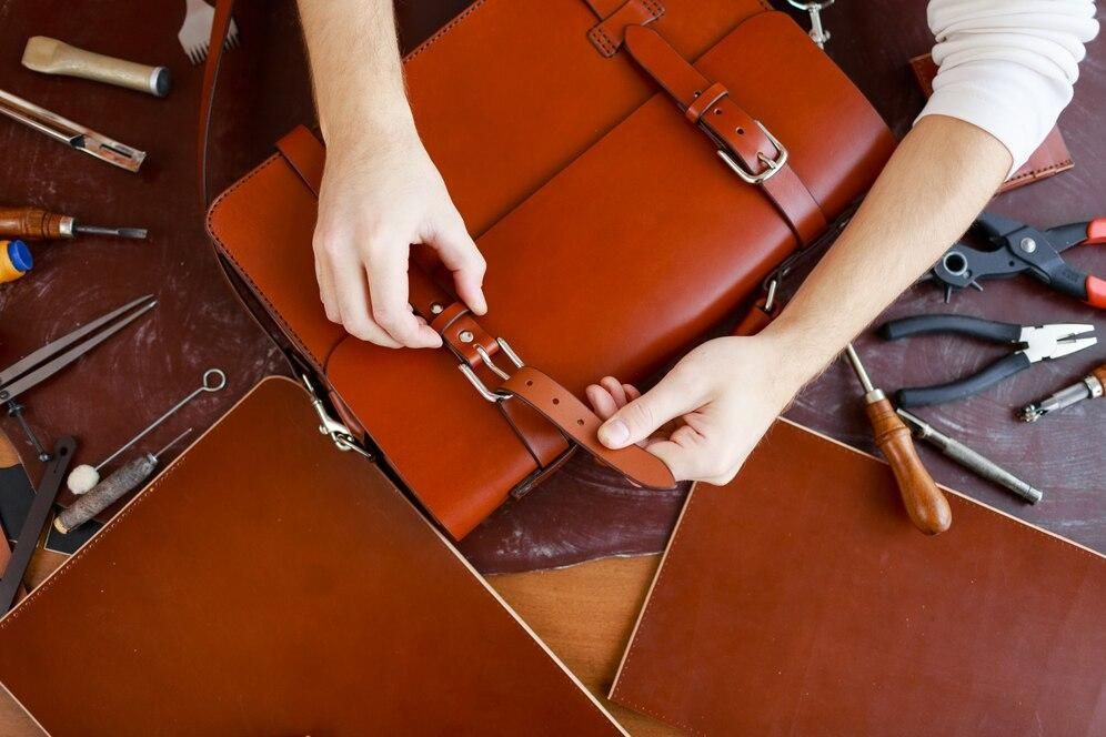 A person is working on a brown leather bag.