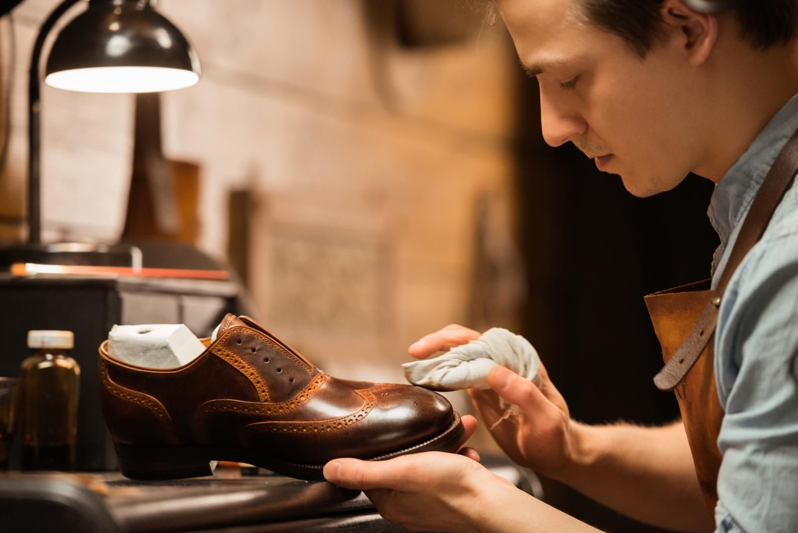 A man is polishing a pair of brown shoes in a workshop.