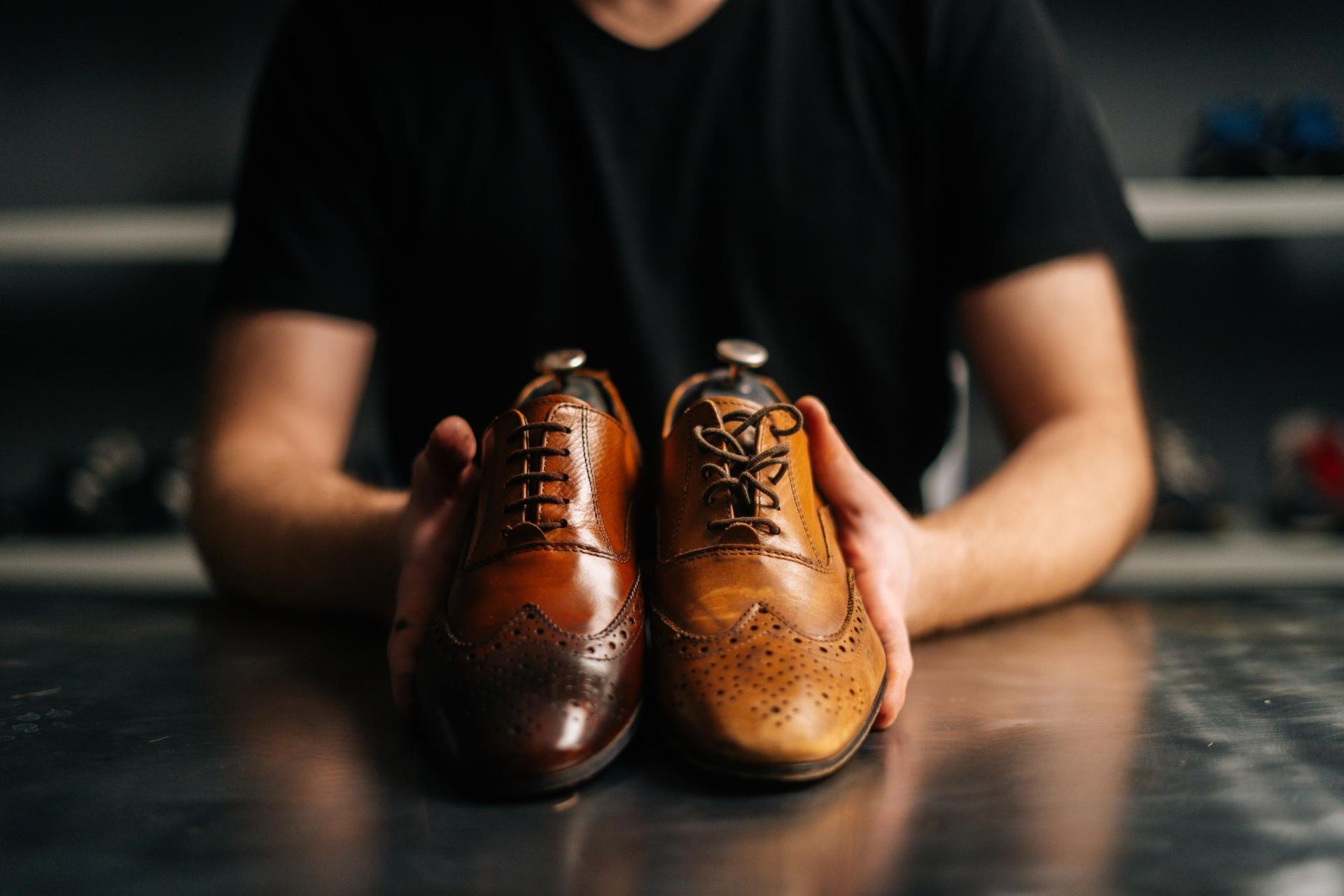 A man is holding two brown shoes in his hands.