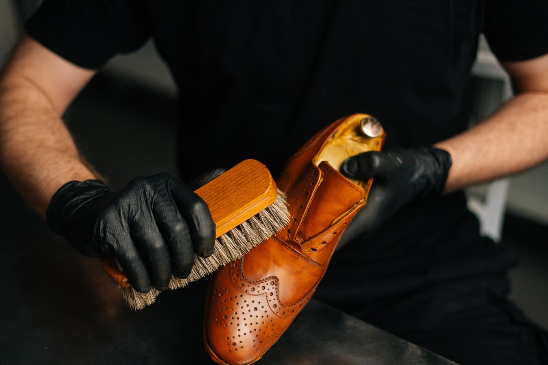 A man is cleaning a pair of brown shoes with a brush.
