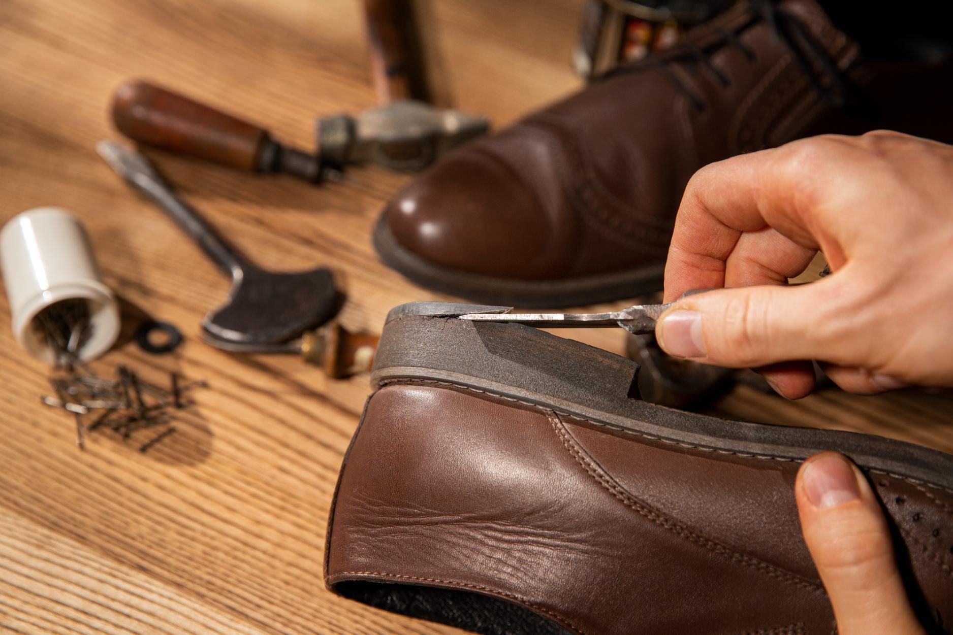 A person is repairing a pair of brown shoes on a wooden table.