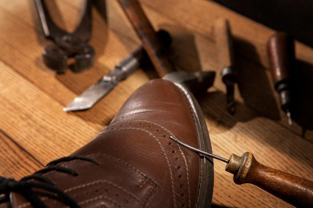A shoe is being repaired with a needle on a wooden table.
