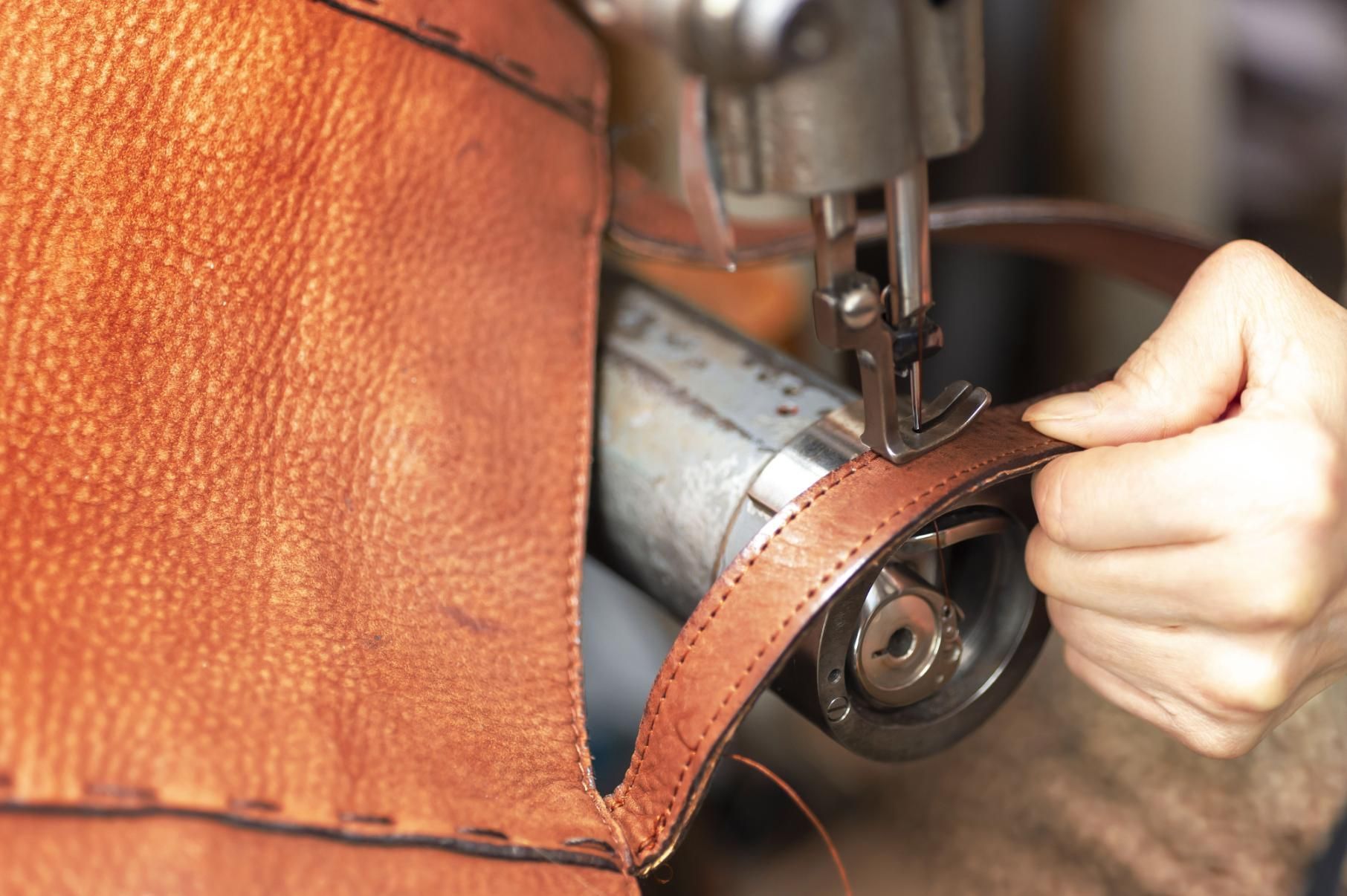 A person is using a sewing machine to sew a piece of leather.