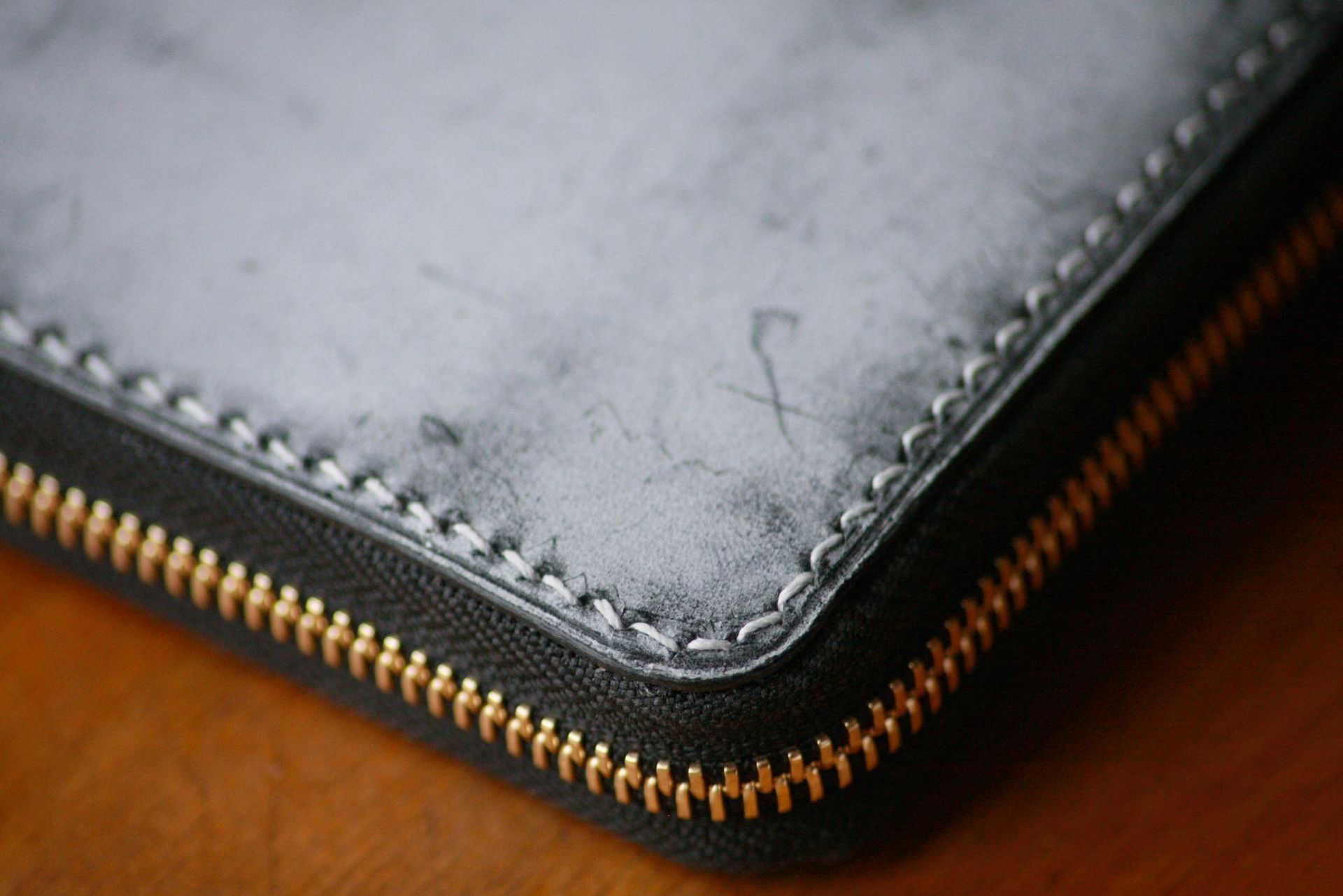 A close up of a black leather wallet with a zipper on a wooden table.