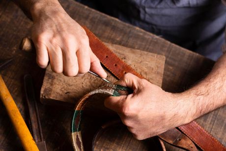 A man is working on a leather belt on a wooden table.