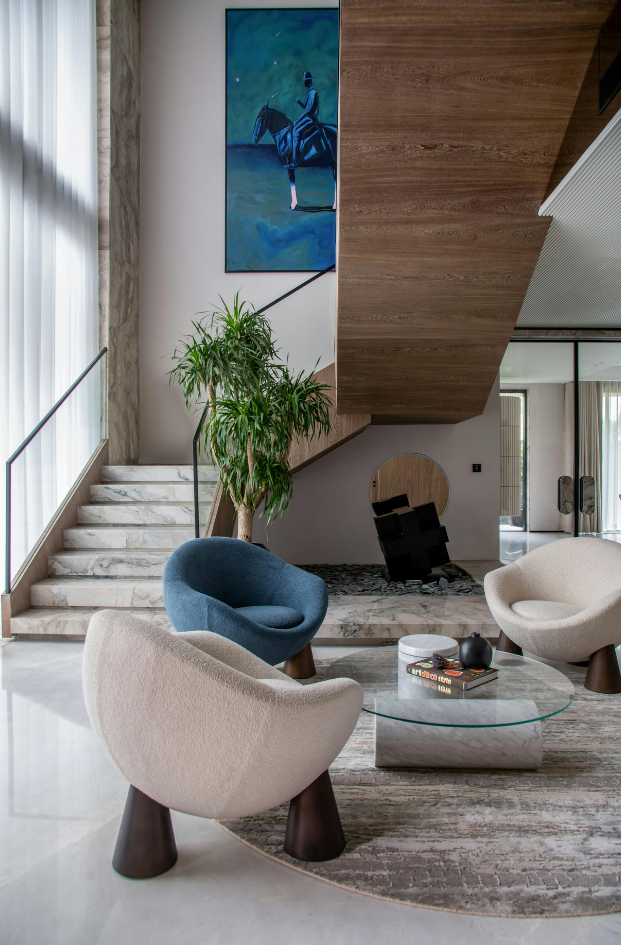 Modern living room with curved lounge chairs, staircase, large plant, and wooden accent wall
