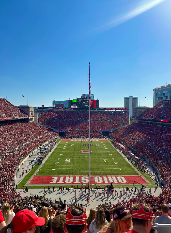 Ohio Stadium packed with fans during a football game, with a clear blue sky overhead and the field centered.