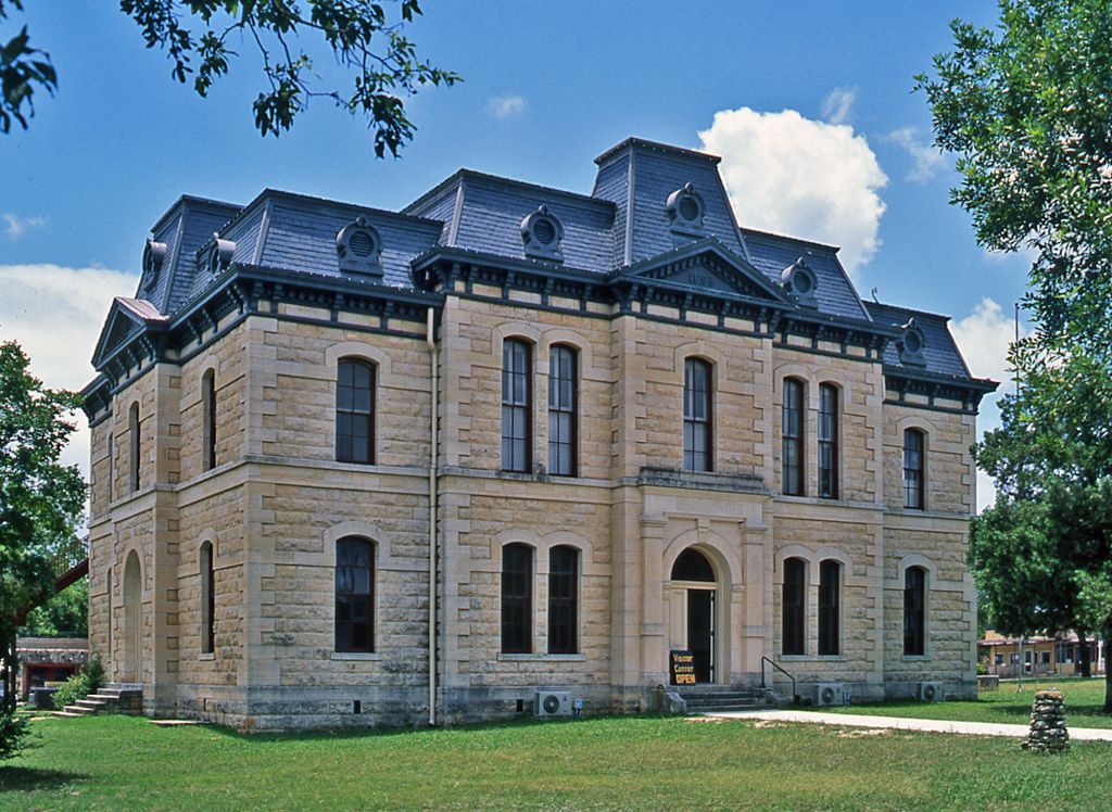 Stone historic mansion with a dark slate roof, framed by trees on a sunny day