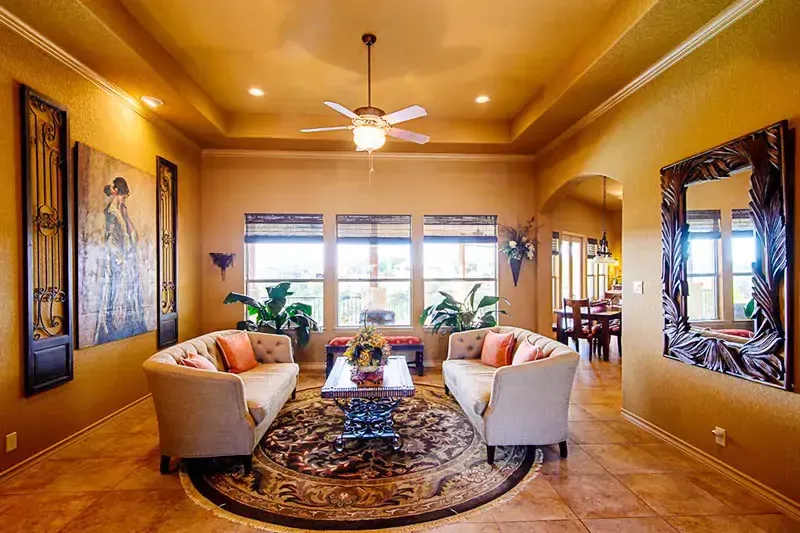 Elegant living room with beige sofas, patterned rug, warm lighting, and large windows.