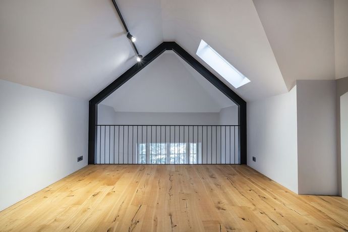 Empty loft space with wooden floor, black metal railing, and skylight.