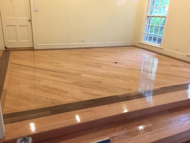 Hardwood floor, diagonal pattern, with dark border. Light-colored walls and door, window on the right.