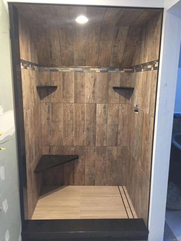 A newly tiled shower with wooden-look tiles, a built-in bench, and black trim.