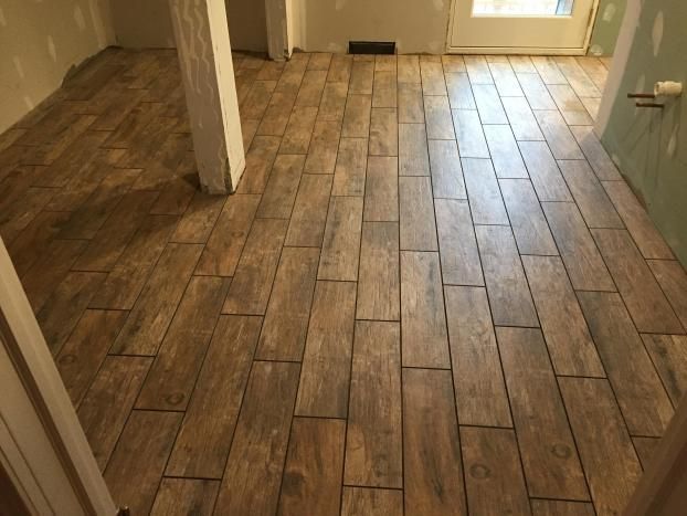 Wood-look tile flooring installed in a room with a white support beam and a doorway.