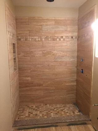 Shower stall with beige horizontal tile, mosaic floor, built-in shelf, and chrome fixtures.