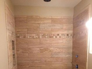 Tiled shower stall with beige rectangular wall tiles and decorative accent band, recessed niche on left.