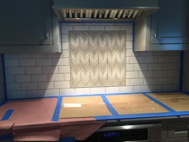 Kitchen backsplash tile installation in progress; countertop taped off with paper and blue tape.
