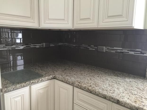 Kitchen corner with white cabinets, speckled countertops, and dark backsplash.