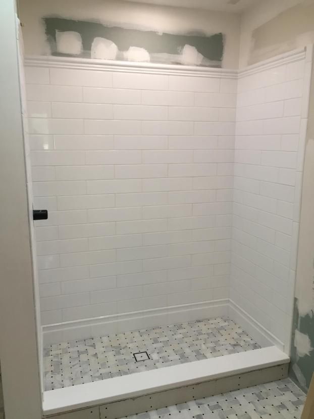 White tiled shower with a gray tiled floor, a white trim, and a black handle.