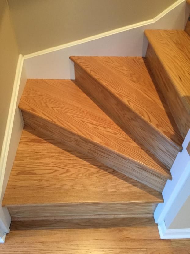 Wooden staircase with three steps, viewed from above, ascending to the right. White trim and tan walls are visible.