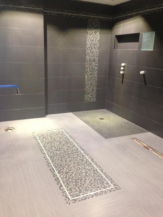 Dark gray tiled shower stall with pebble accent strips and drainage.