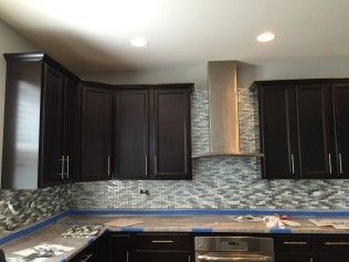 Dark kitchen cabinets with a mosaic backsplash and stainless steel range hood.