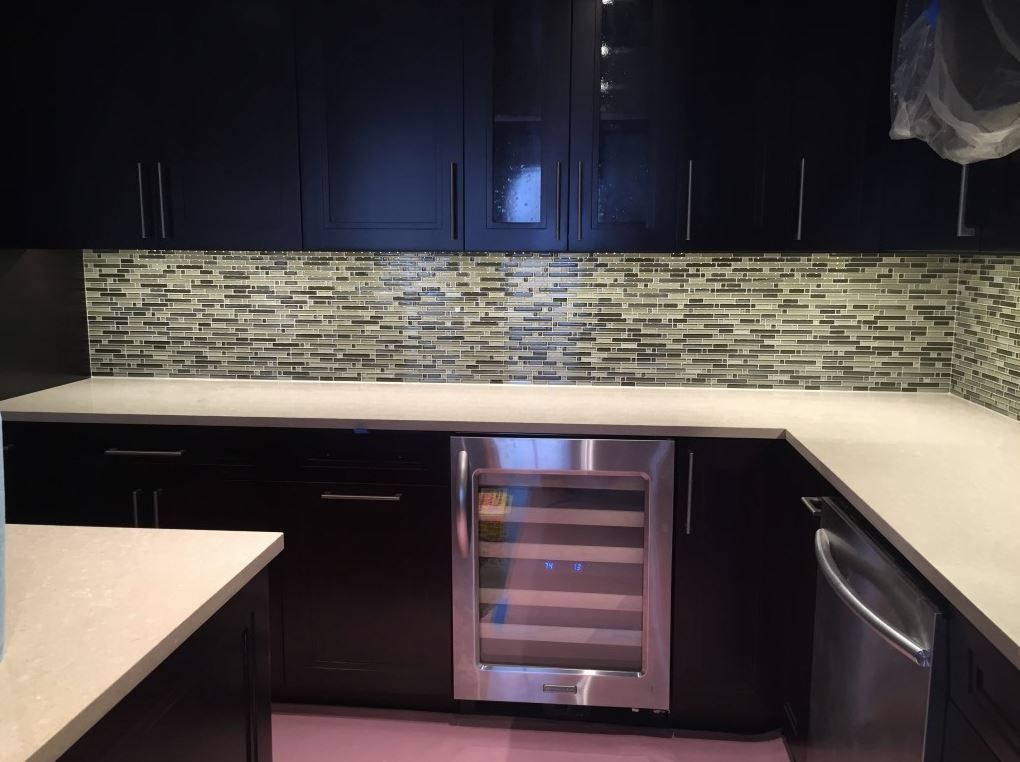 Dark wood kitchen cabinets with light countertops and a mosaic tile backsplash. A wine fridge is built-in.
