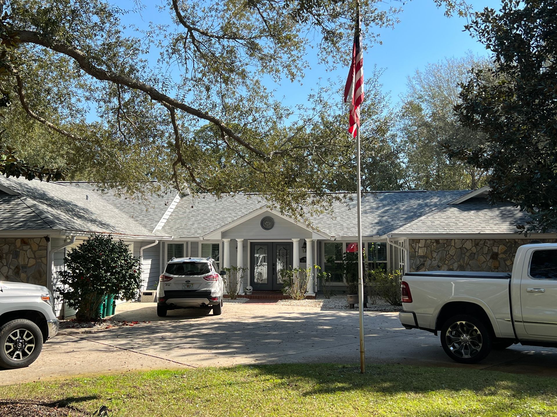 House exterior with stone accents, vehicles in driveway, American flag.