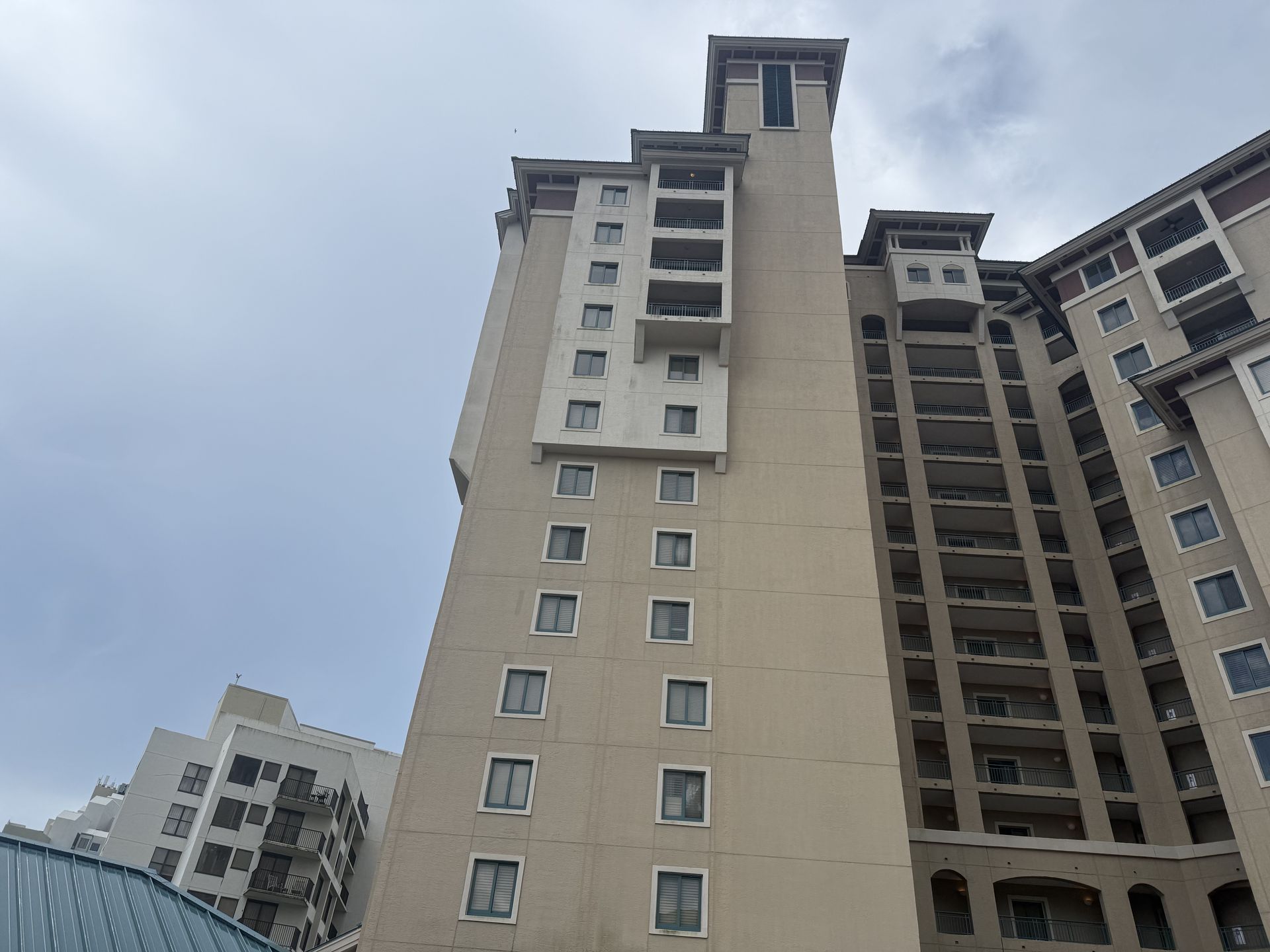 Tall beige building with many windows under a cloudy sky.