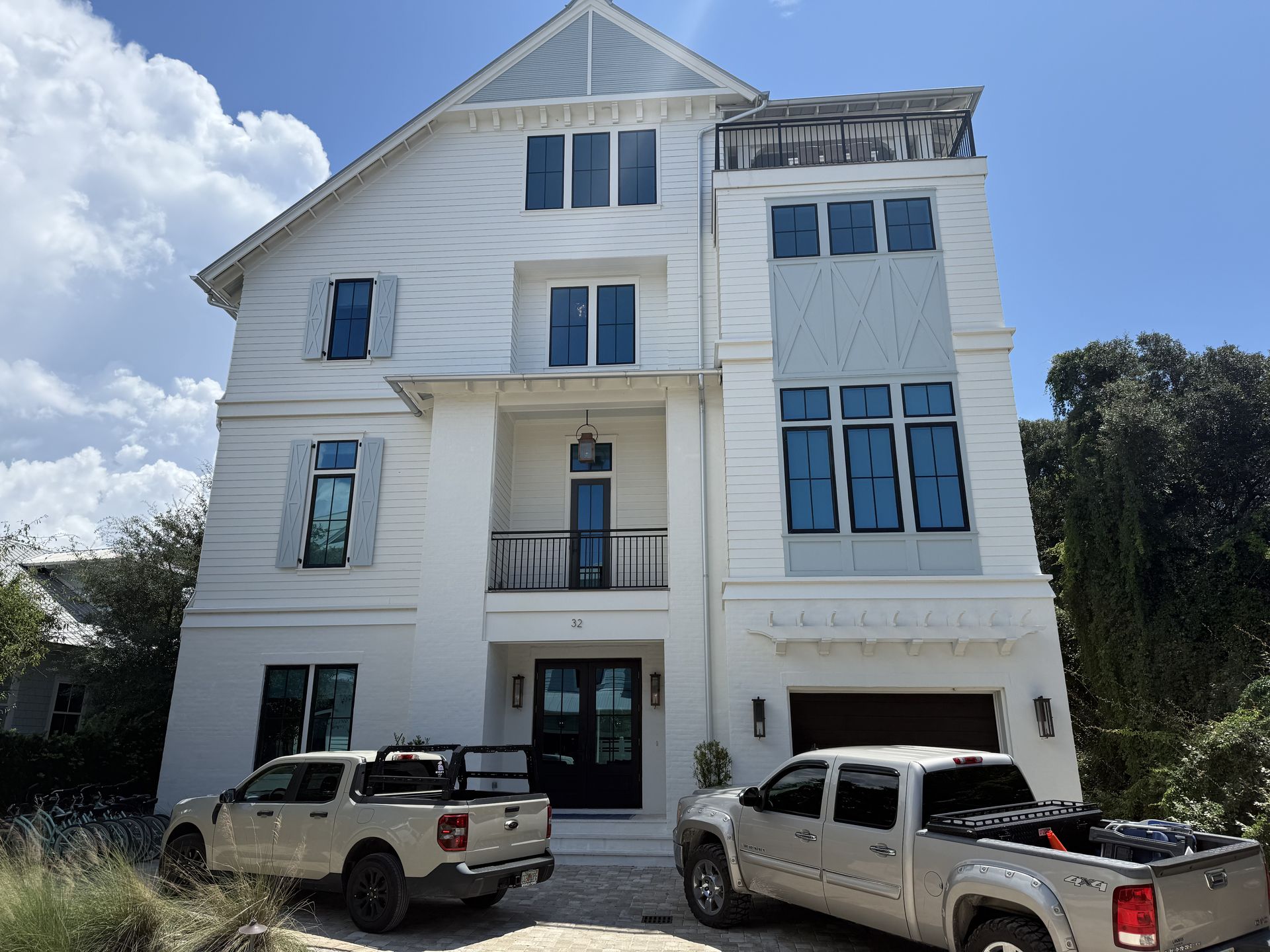 White multi-story house with blue-tinted windows, two trucks parked in front, clear sky.