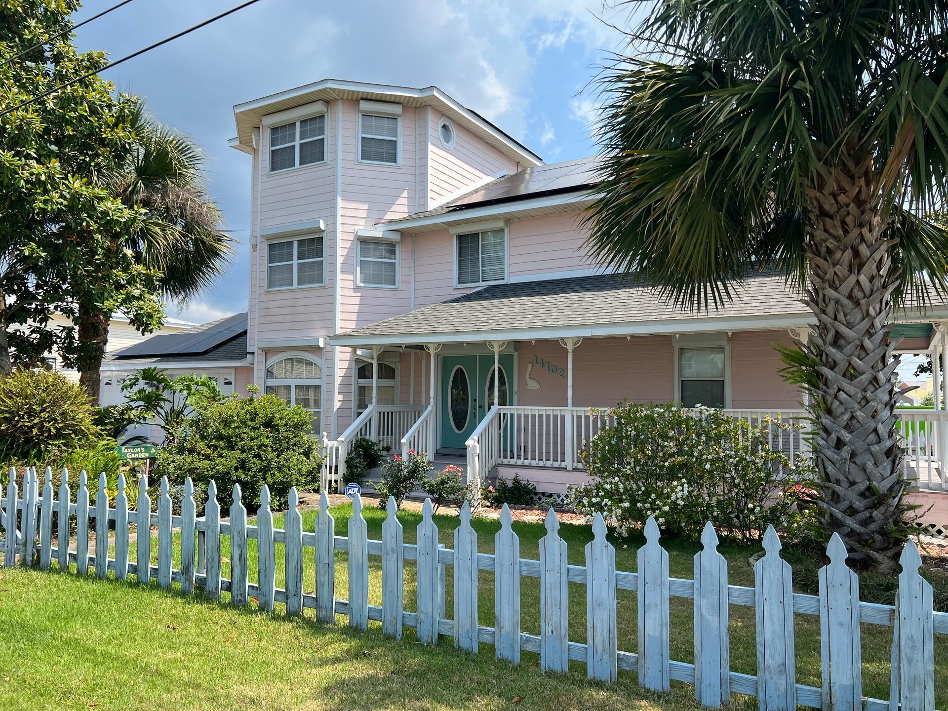 Pink house with white picket fence, palm trees, and blue front door.