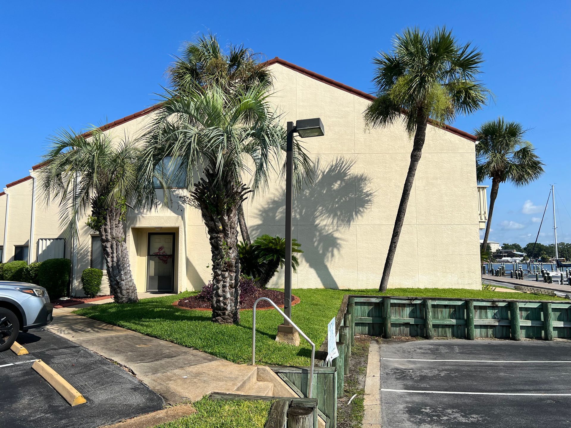 Beige building with palm trees, grass, and parking lot. Clear blue sky.