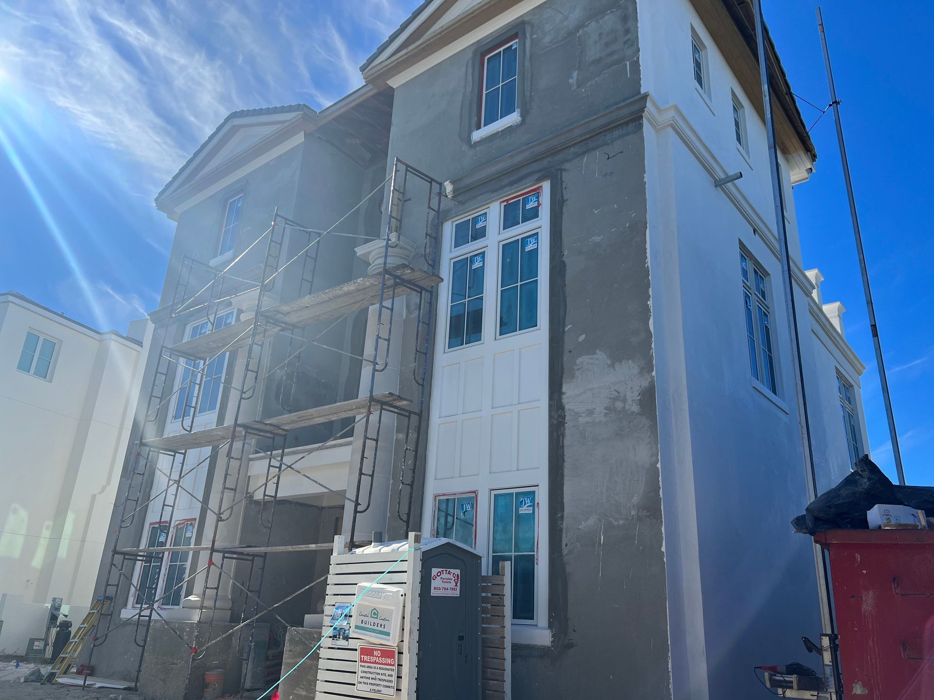 Building under construction with scaffolding, plaster, and white trim against a bright blue sky.